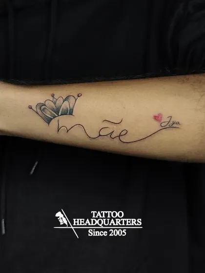 A tattoo that reads "mãe" (Portuguese for mom) with a crown, and "Jya" with a heart, a beautiful tribute to family.