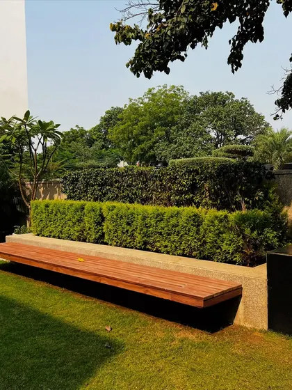 A floating wooden bench provides minimalist seating in this quiet corner of the garden. This custom hardscaping element is set against a backdrop of layered hedges, creating a peaceful spot for reflection.