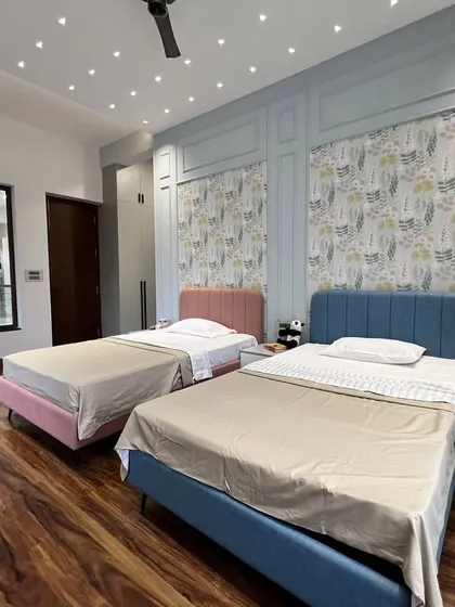 This angle shows the twin beds and the large internal window that connects to another space, making the room feel more open. The combination of wood flooring and pastel colors creates a warm and inviting environment.