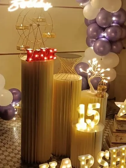 A closer look at the details for Varsha's 15th birthday. The setup includes tiered pedestals for the cake, a light-up number '15', and other props like a lit star and decorative suitcases to add personality.