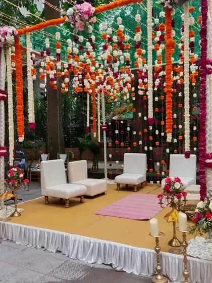 This mandap features a canopy of hanging marigold and tuberose strings, creating a vibrant and festive atmosphere. The simple white seating provides a beautiful contrast to the colorful floral display.