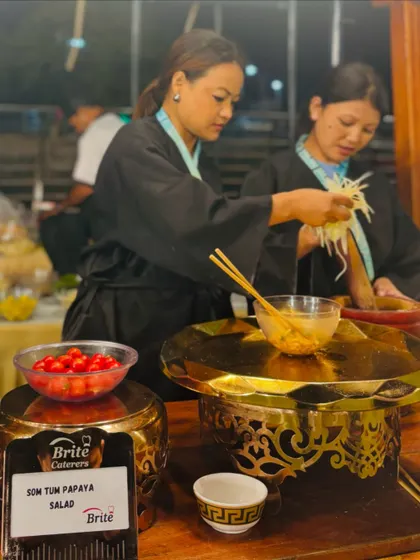 Chefs at the live Thai station preparing Som Tom Papaya Salad, using a traditional mortar and pestle to combine fresh ingredients.
