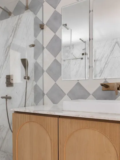 This elegant bathroom features a custom wood vanity with arched, reeded door panels. The walls are a mix of diamond-patterned marble tiles and a large marble slab, creating a rich, textural look.