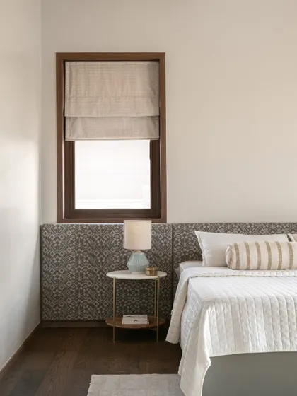 A detail of the primary bedroom, showing the patterned fabric headboard and a simple, elegant bedside table. The textures and tones are chosen to create a restful and serene environment.