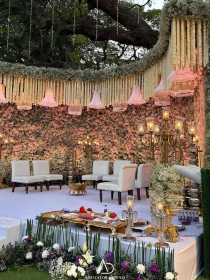 A detailed look at the wedding ceremony stage, with its floral wall, traditional lamps, and elegant white seating for the family.