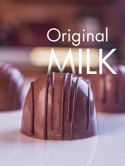 Our Original Milk praline appears beneath a chocolate drizzle, with its curved moulded shape shown close up.