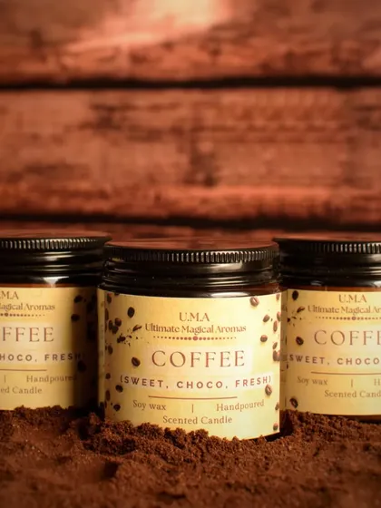 A trio of my 'Coffee' scented candles in their amber jars, set against a backdrop of coffee grounds. The label design is simple and rustic to match the scent.
