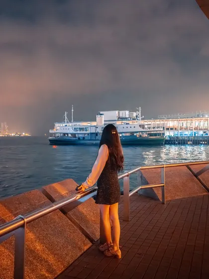 A lone figure watches a ferry from the Tsim Sha Tsui promenade. This shot captures a quiet, contemplative moment amidst the grandeur of the city.