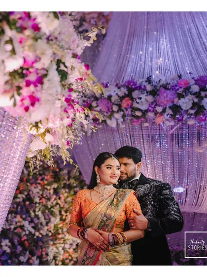 A stunning portrait of the couple at their reception, surrounded by a breathtaking floral and crystal decor setup. The purple lighting adds a touch of royal glamour.
