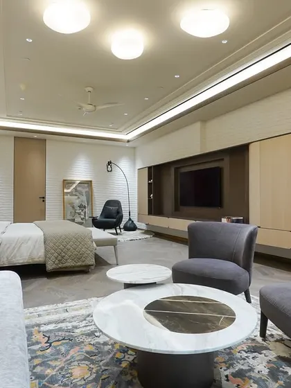 A wide view of a spacious master bedroom that combines sleeping and living areas. The custom furniture, including the bed, daybed, and armchairs, is arranged to create a multi-functional yet cohesive retreat.