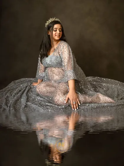 An artistic maternity portrait with a water reflection effect. The mother-to-be is seated in a shimmering silver gown, creating a serene and magical image.