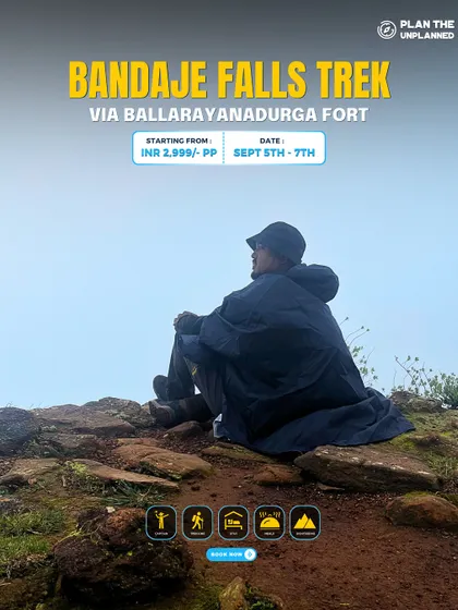 A trekker in a poncho sits atop a rocky outcrop on the way to Bandaje Falls, surrounded by fog. This is the moody beauty of a monsoon trek.