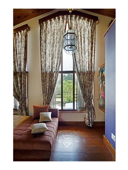 This cozy nook in a bedroom features a daybed set against a large window with high ceilings. The use of patterned curtains and warm wood flooring creates a comfortable, intimate space for rest and contemplation.