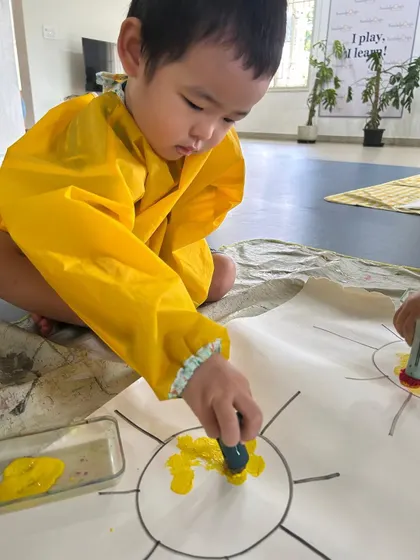 Dressed in a yellow smock, this child shows intense concentration while painting. We provide a safe space for children to get messy and fully engage in their art.