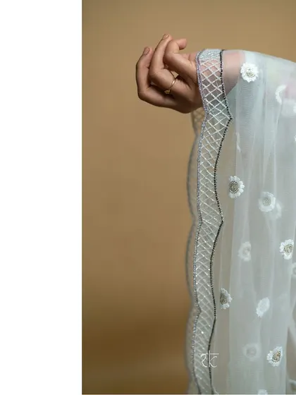 A detail shot of the baby blue ensemble's tulle scalloped dupatta, featuring delicate floral embroidery that adds a touch of ethereal beauty.