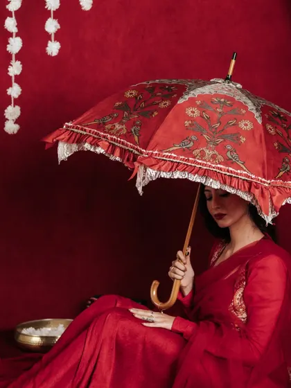 This seated pose offers a different perspective, showing how the umbrella can be used as a prop in various lifestyle scenarios. The composition is quiet and contemplative, focusing on the product's beautiful bird and floral motif.