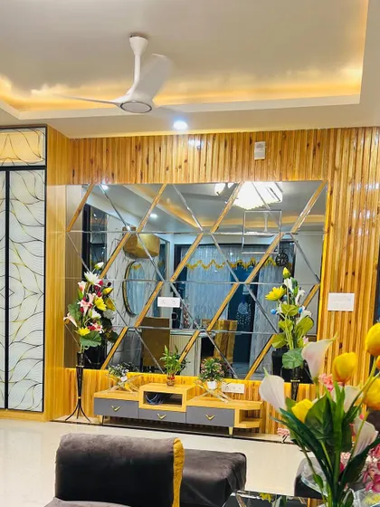 A finished living room with a TV unit set against a wall of beveled mirrors and wood paneling. The space is decorated with flowers, ready for the client to enjoy.