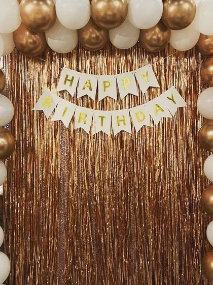 A classic birthday backdrop with a gold fringe curtain. A 'Happy Birthday' banner is framed by a simple yet elegant white and gold balloon arch.