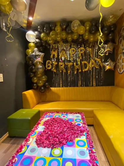 A birthday party in a cafe with a black and gold balloon decoration and a table decorated with rose petals.