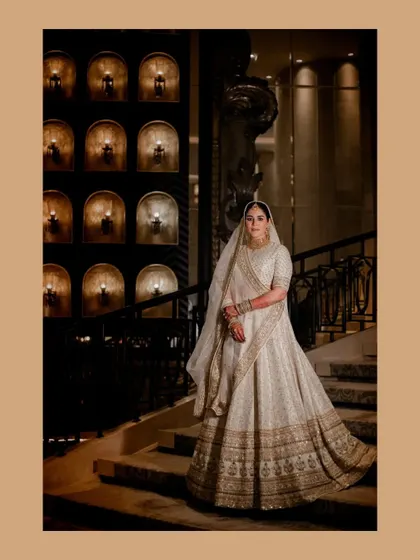 A full-length portrait of the bride on a grand staircase, her white lehenga creating a stunning visual.