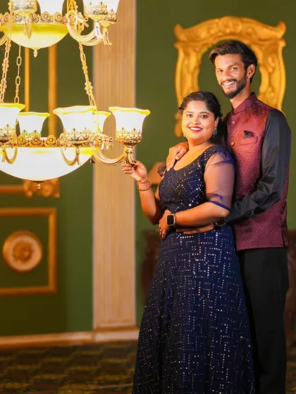 A regal-looking pre-wedding photo in a luxurious room with a grand chandelier. The couple's formal wear perfectly matches the opulent setting.