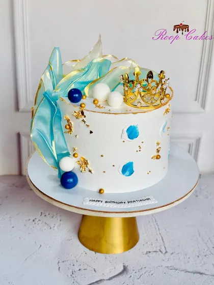 Royalty in every bite. This stunning cake features abstract blue sails, a golden crown, and artistic paint strokes for a modern and regal look.