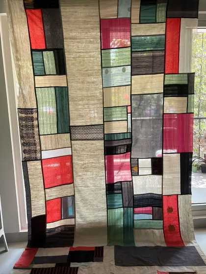 A full view of a Pojagi room divider, made from sarees and dhotis. The semi-transparent fabrics create a beautiful, light-filtering effect.
