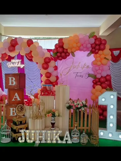 A warm and inviting first birthday setup for Juhika. The red, pink, and orange balloon arch creates a cheerful and bright backdrop.