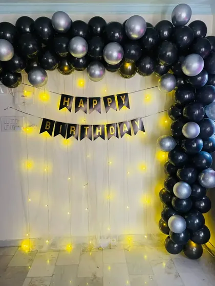 A simple and chic black and silver balloon arch. This decoration is paired with a 'Happy Birthday' banner and a curtain of fairy lights.