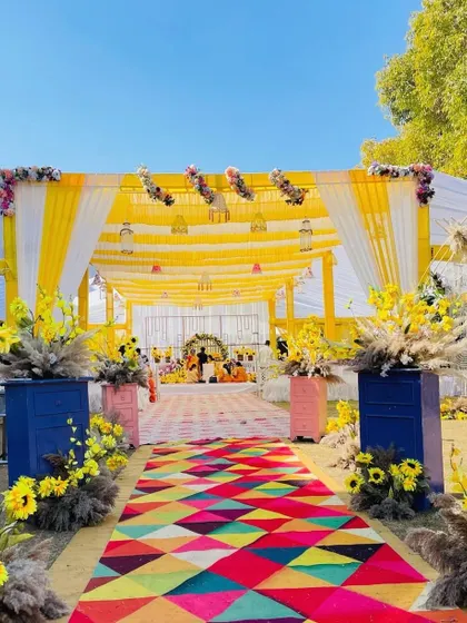 A closer look at the colorful entrance aisle for a Haldi event. The bright runner contrasts beautifully with the blue and pink planters holding yellow flowers.