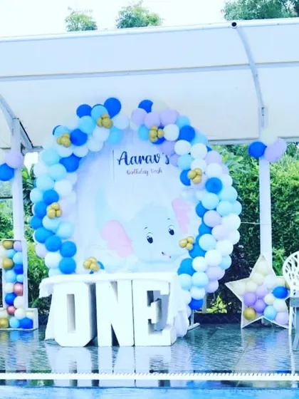 An outdoor birthday party setup by a pool with an elephant theme. The blue and white balloon arch and 'ONE' table create a beautiful and refreshing look.