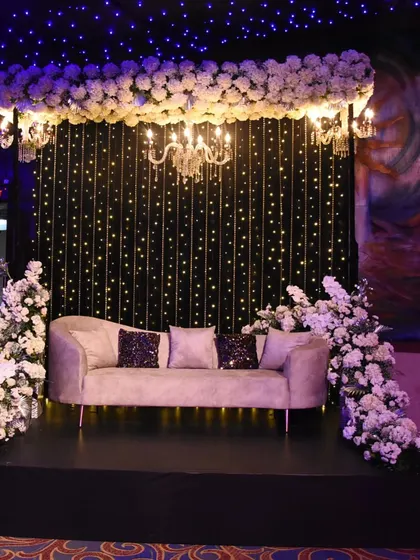 An intimate and elegant photo spot with a 'starry night' theme. A plush couch is set against a backdrop of twinkling lights, framed by white florals and a classic chandelier.