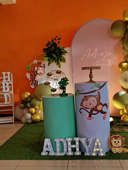 A playful monkey-themed third birthday party. The decor features cute monkey cutouts, a green and gold balloon arch, and a faux grass floor.