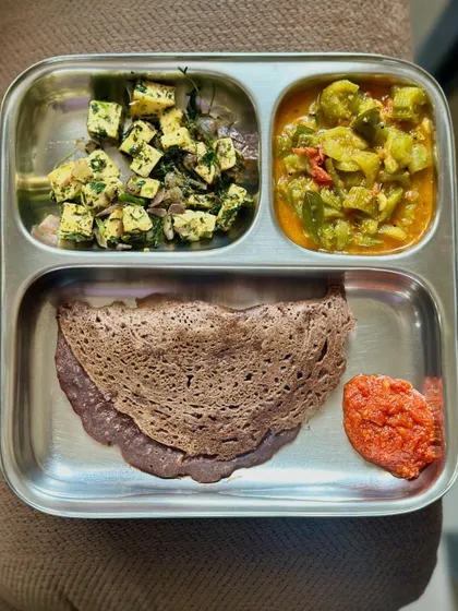 This plate features a ragi dosa with sautéed paneer, mixed vegetable curry, and a spicy tomato chutney.