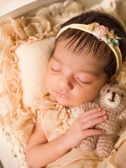 A tiny angel sleeping with her teddy bear. This close-up shot highlights the delicate features of the newborn, her floral headband, and the sweet little prop, creating a precious memory.
