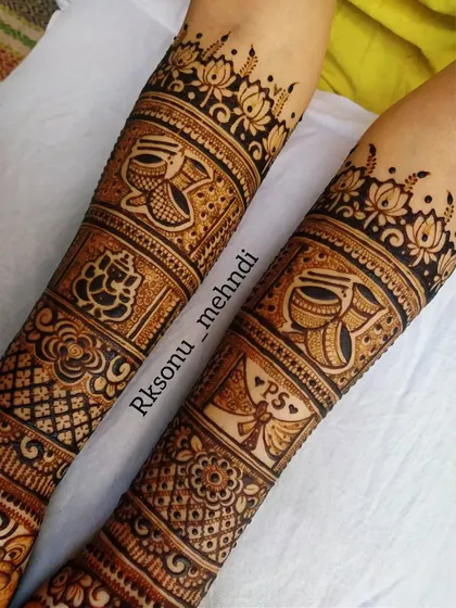 A close-up of the arm portion of a full bridal design. This image highlights the detailed panels containing auspicious symbols like Ganesha, kalash, and a wedding invitation with the couple's initials.
