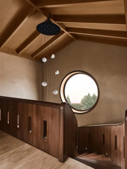 Looking down the spiral staircase from the upper level, this view shows the relationship between the wooden structure, the round window, and the pendant lighting, creating a harmonious architectural moment.