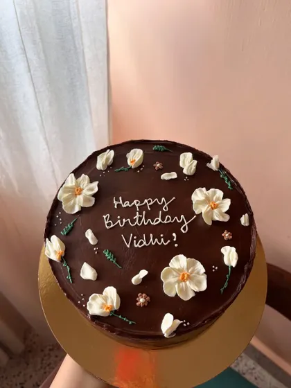 A rich chocolate ganache cake providing a beautiful dark canvas for delicate, hand-piped white buttercream flowers.