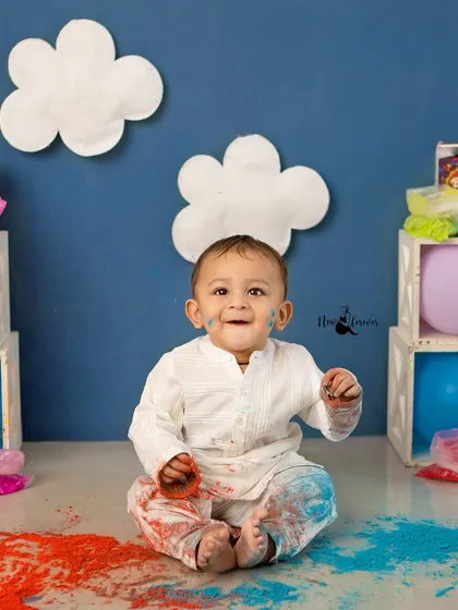 A baby boy in a white kurta enjoying the colorful mess of his first Holi photoshoot.