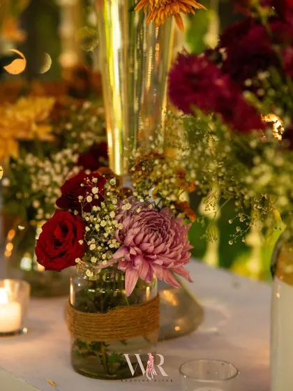 A rustic centerpiece in a jute-wrapped jar, featuring a mix of roses, chrysanthemums, and baby's breath. This simple detail perfectly encapsulates the event's bohemian charm.