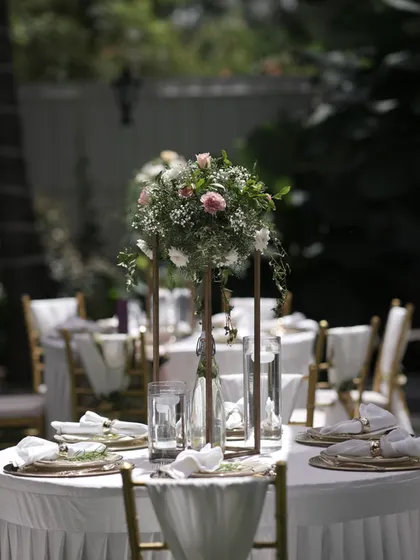 A beautiful outdoor table setting with a tall floral centerpiece, creating an elegant and airy feel for a daytime reception.