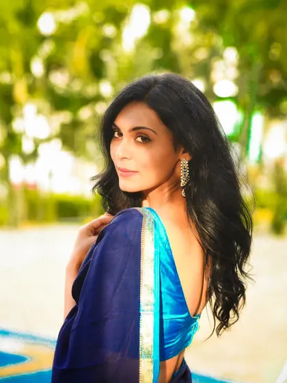 A classic over-the-shoulder pose in a blue saree. This outdoor shot highlights her elegant profile and the beautiful drape of the fabric.