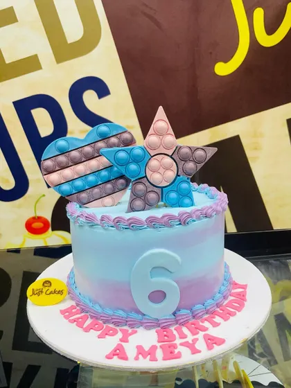 A 1.5kg Pop It theme cake in pastel pink and blue, with heart and star toppers.