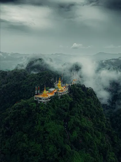 The famous Tiger Cave Temple perched on a mountain in Krabi, surrounded by clouds. A challenging climb with a rewarding, spiritual view.