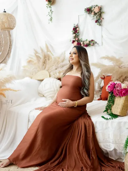 A serene portrait in a rustic, boho-chic setting. The mom-to-be's earthy-toned gown and the natural decor create a calm and beautiful image.