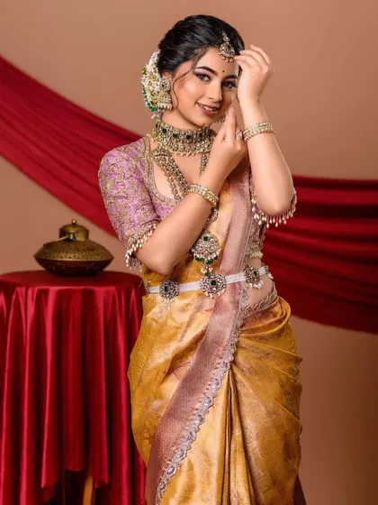 A full-length portrait showcasing a royal and elegant look. The combination of a golden-yellow saree and a lavender embroidered blouse creates a unique and regal appearance, perfect for a grand occasion.