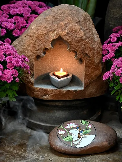 A natural stone lamp with a niche for a diya, placed next to a hand-painted stone. This handcrafted piece is inspired by the rich culture and traditions of our past, perfect for the festive season.