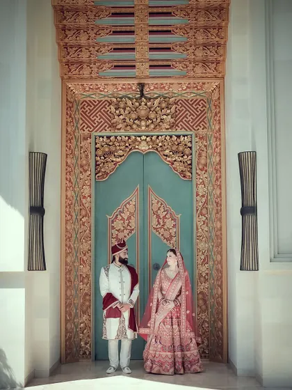A grand and symmetrical shot of a couple standing before an ornate, beautifully carved doorway, creating a regal wedding portrait.
