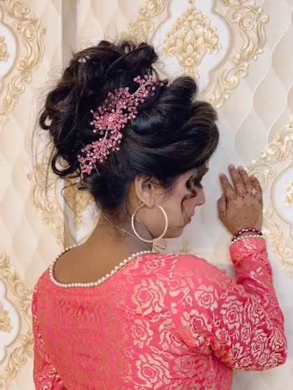 A side profile of an elegant party updo. This messy bun is decorated with a beautiful pink hair accessory, perfect for a reception or engagement.