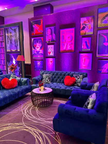 A cozy lounge for a love-themed party, with blue velvet sofas, heart-shaped cushions, and a gallery wall of romantic and pop-art posters.
